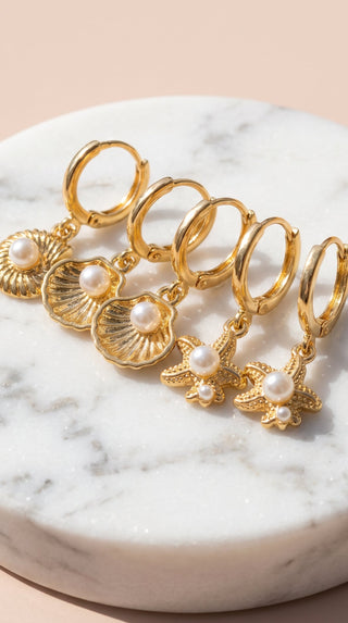 Set of gold hoop earrings with pearls on a marble surface